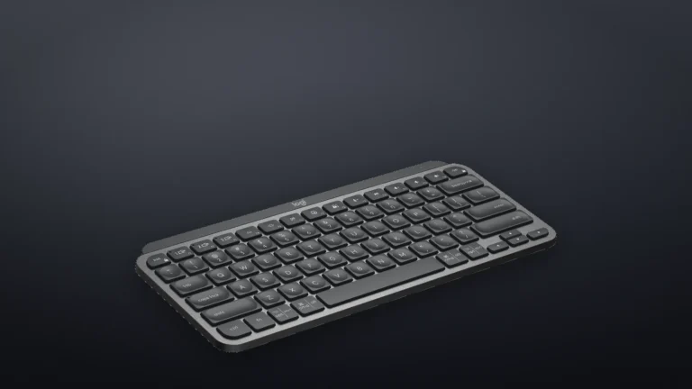 Logitech MX Keys Mini Graphite așezată plat, văzută din lateral-față, pe un fundal închis la culoare